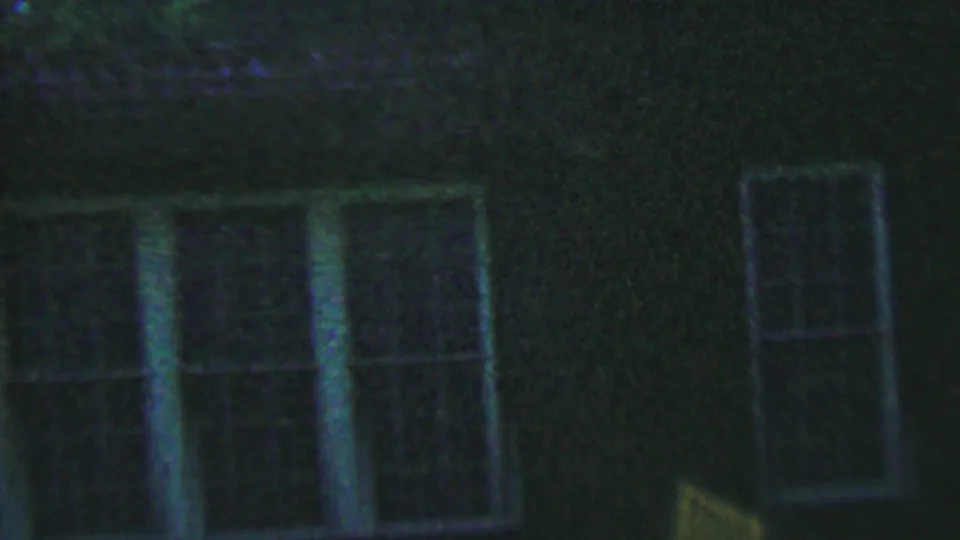 1956 Hatfield, Pennsylvania 8mm frame showing a dark exterior wall with a large multi-pane window section, pale vertical trim, and a smaller rectangular window at right.