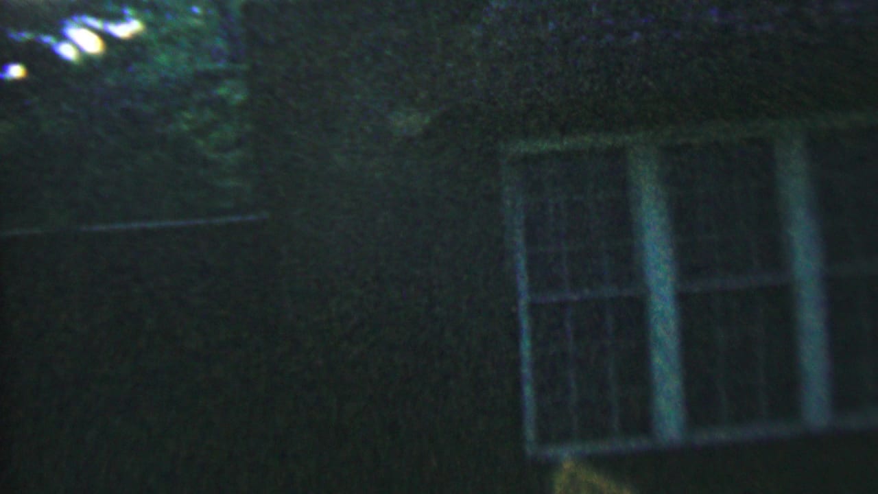 Dim upper portion of a house with white window frames and tree shadow.