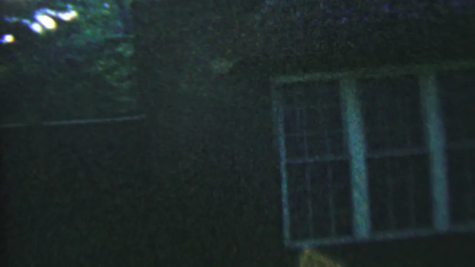 1956 Hatfield, Pennsylvania 8mm frame of the upper house facade at night, with white window frames partly obscured by darkness and foliage.