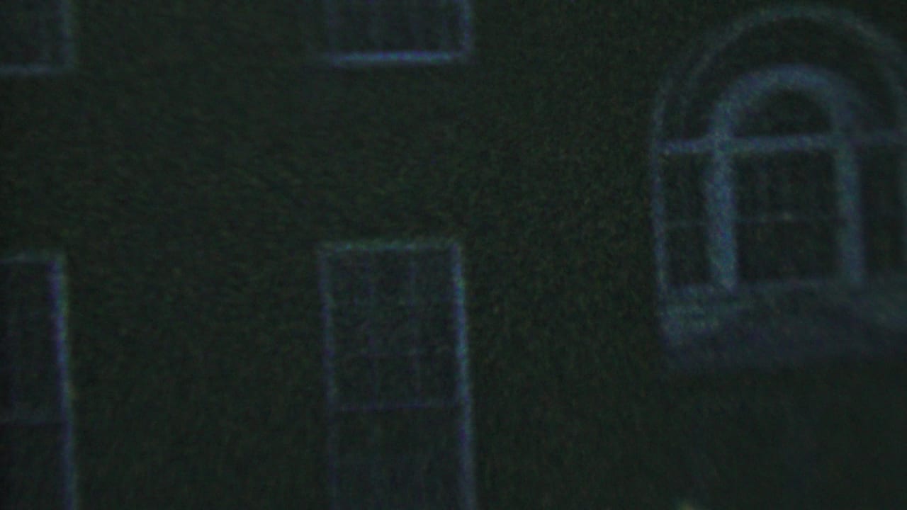 Low-light 1956 8mm frame from Hatfield, Pennsylvania showing a dark brick building facade with rectangular window openings and pale trim.