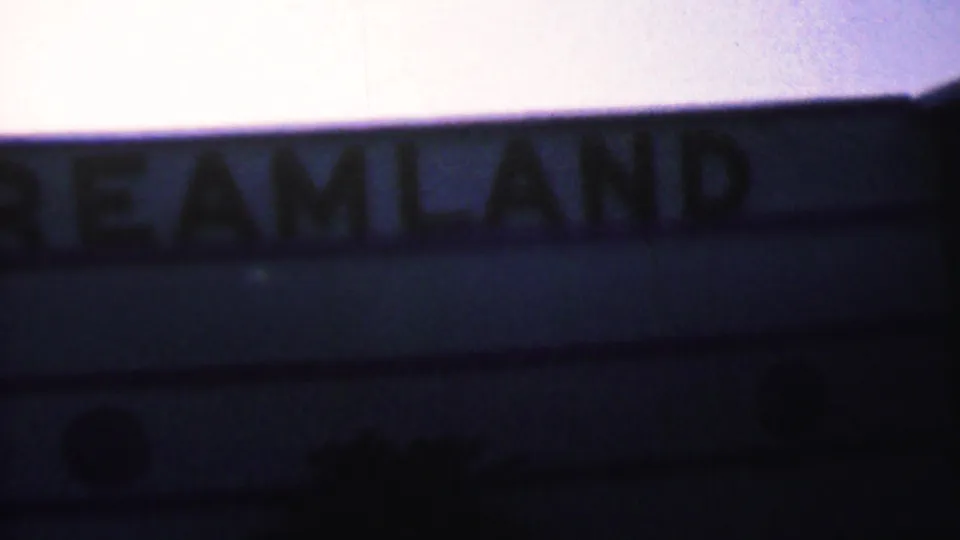 Close, dark 8mm view of the Dreamland lettering on a building or marquee edge, with the surrounding structure mostly in shadow.