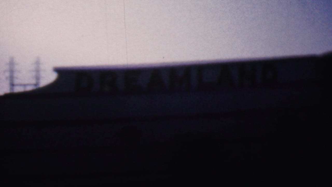 1956 Hatfield, Pennsylvania 8mm frame showing a low building roofline and partially visible DREAMLAND lettering in deep shadow against a dusky sky.
