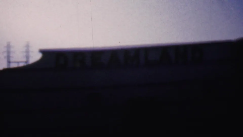 1956 Hatfield, Pennsylvania 8mm frame showing a low building roofline and partially visible DREAMLAND lettering in deep shadow against a dusky sky.