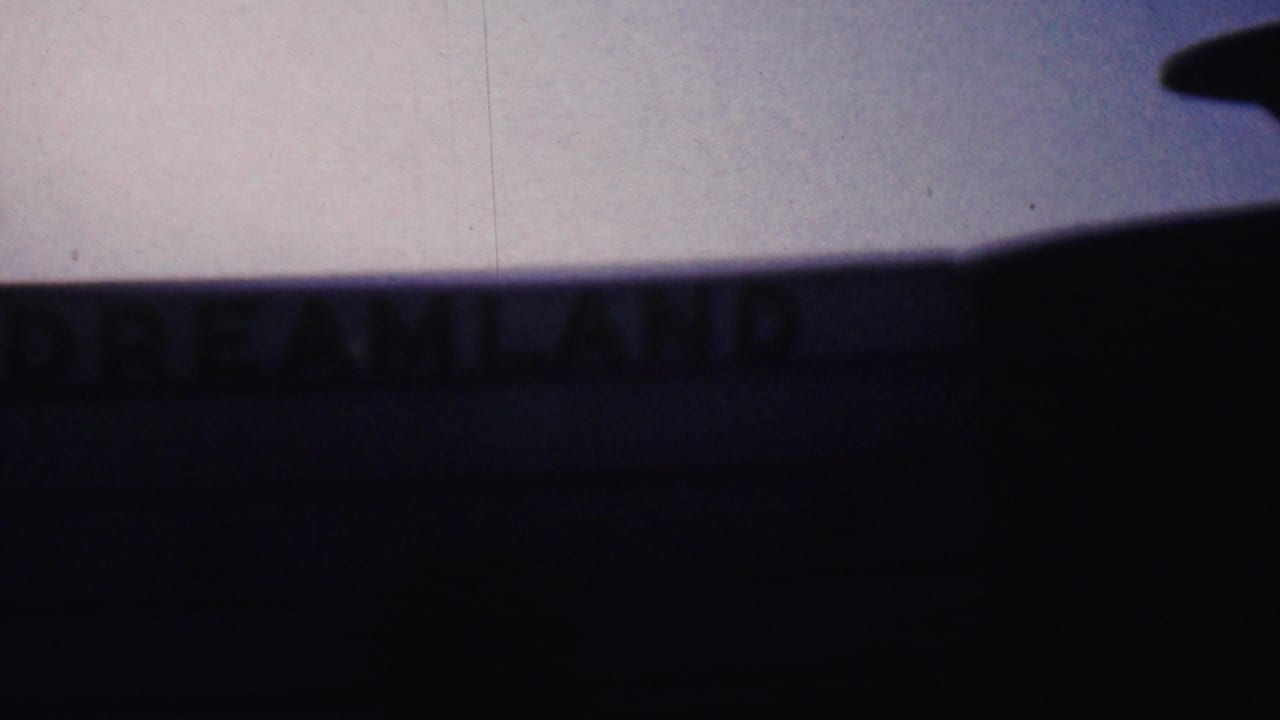 Blurred dark building facade with DREAMLAND letters across the upper edge.