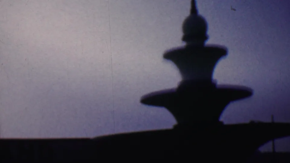 A dark, tiered stone monument or fountain-like landmark stands against the dusky sky in the 1956 Hatfield home-movie footage.