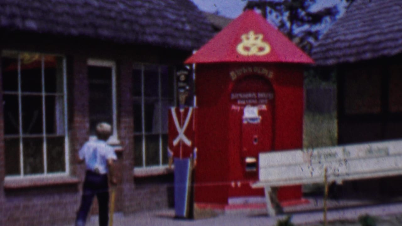 Walker passing a red kiosk, toy soldier figure, and white bench in front of shop buildings.