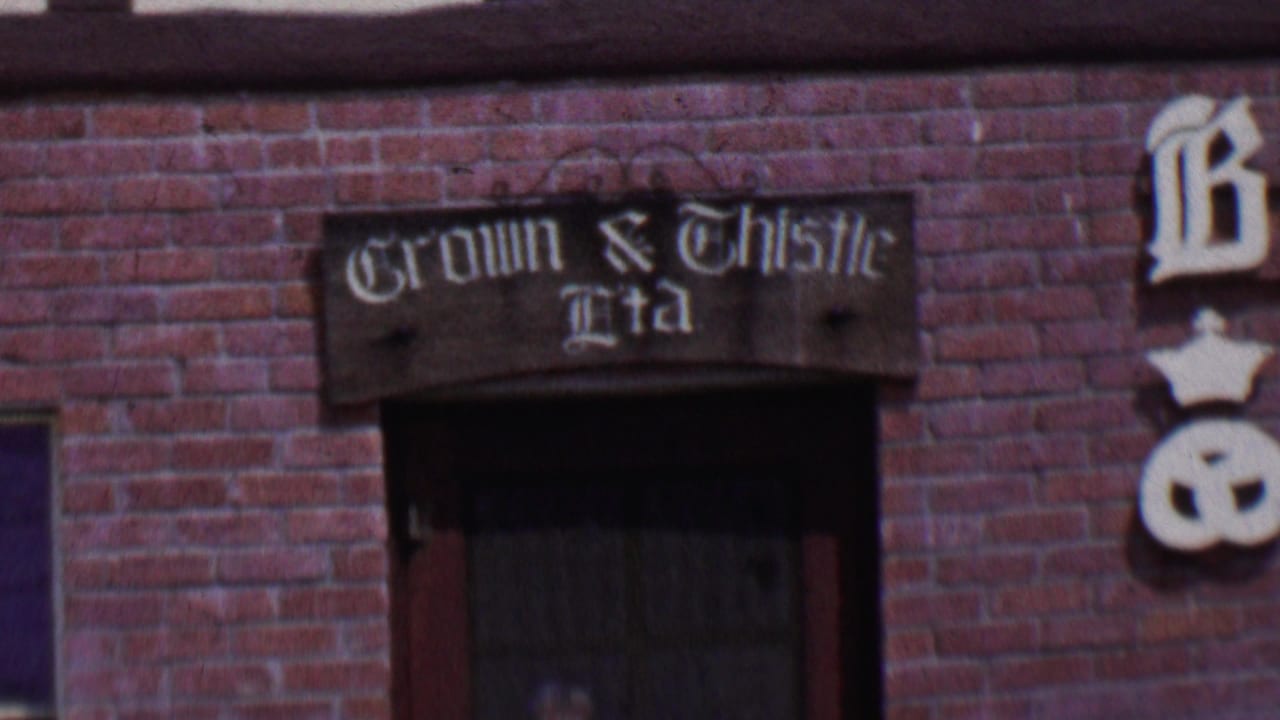 1955 Solvang, California 8mm frame showing a red brick facade with a dark window and a painted Crown & Thistle Ltd sign above it.