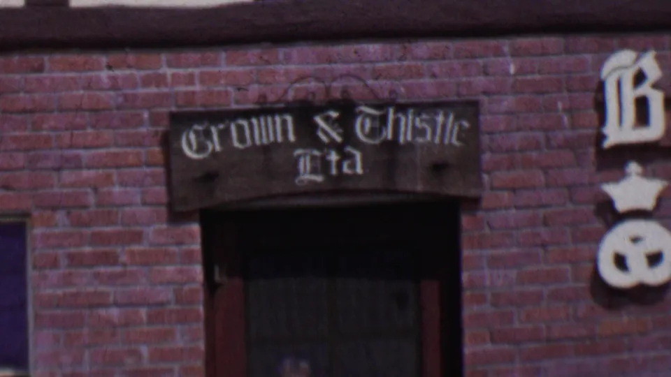 1955 Solvang, California 8mm frame showing a red brick facade with a dark window and a painted Crown & Thistle Ltd sign above it.