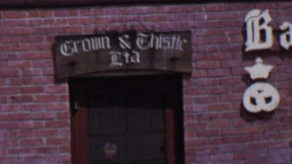 1955 Solvang, California frame with a closer handheld view of the Crown & Thistle Ltd sign mounted over a dark window in a brick facade.