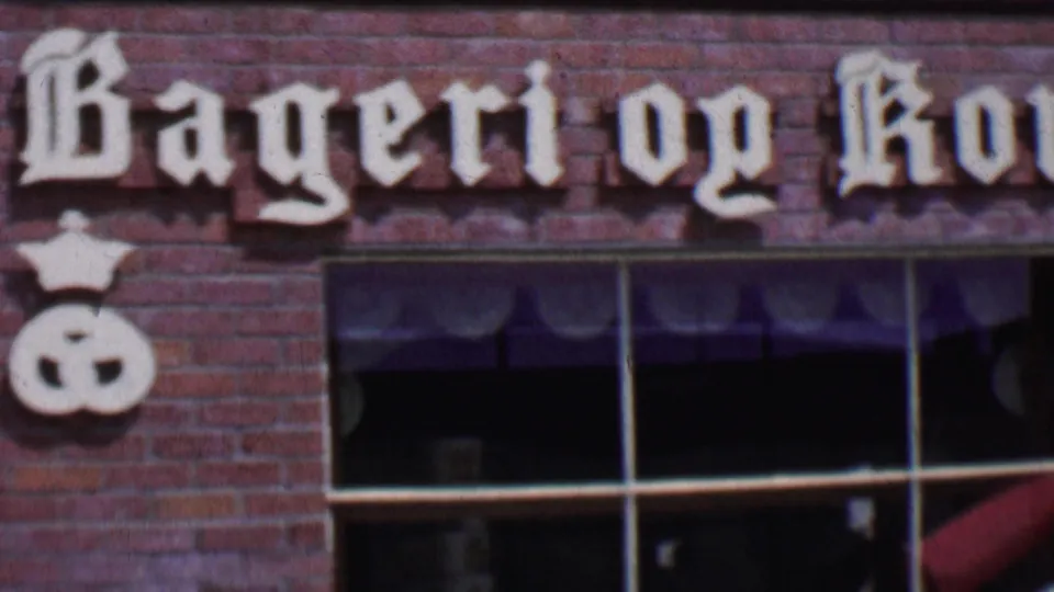 1955 Solvang, California 8mm frame centered on the Bageri og Konditori storefront lettering, with white bakery symbols mounted above multi-pane windows.
