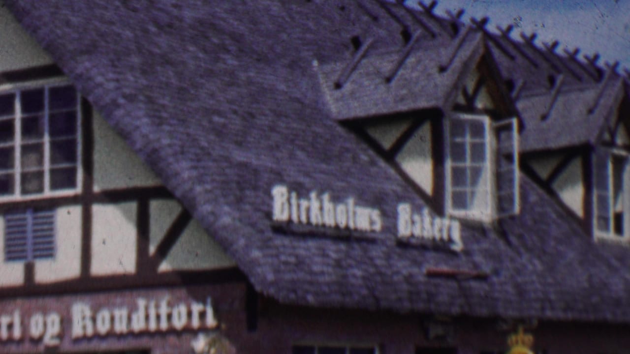 1955 Solvang, California home-movie frame showing Birkholm's Bakery signage on a steep roof with dormer windows and half-timbered facade details.
