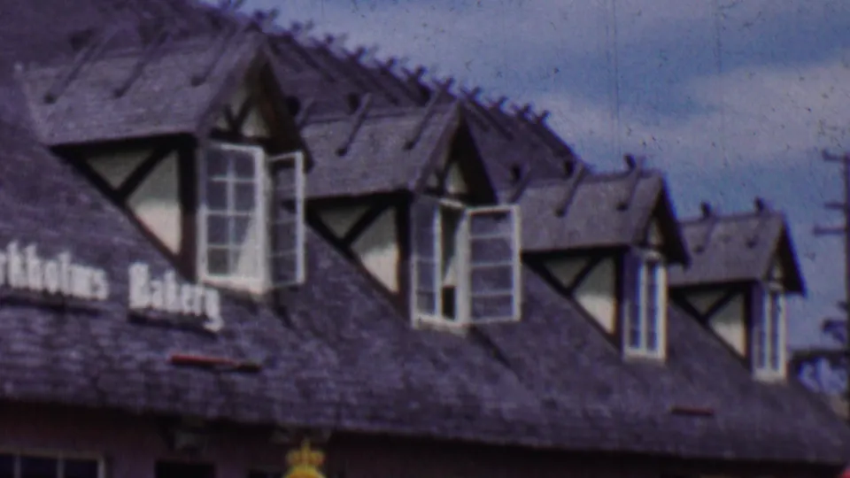 1955 Solvang, California home-movie frame showing the Birkholm's Bakery roofline, multiple dormers, half-timbered trim, and partial storefront signage.