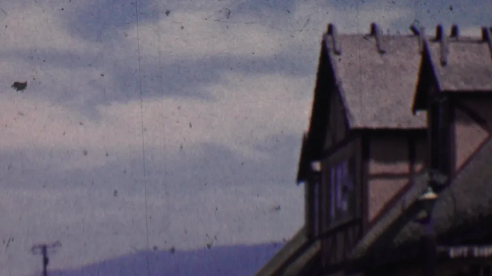 A soft 8mm frame from Solvang shows Danish-inspired half-timbered gables, steep roof peaks, distant hills, and a cloudy sky.