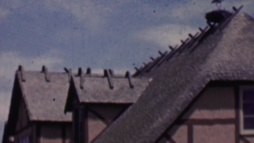 A final 1955 Solvang home-movie frame shows a steep thatch-like roof, half-timbered wall sections, roof ridge details, and muted blue-gray sky.
