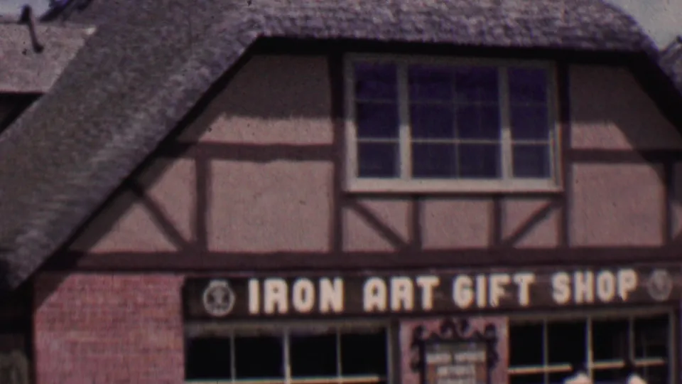 1955 Solvang, California frame showing the IRON ART GIFT SHOP sign below a Danish-style timber-frame facade, brick storefront, windows, and steep thatched roof.