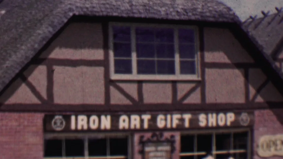 Solvang, California storefront view from 1955 showing the Iron Art Gift Shop sign, half-timbered facade, thatched roof, and large display windows.