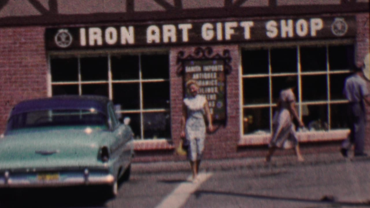 Turquoise 1950s car parked outside the Iron Art Gift Shop as pedestrians pass.