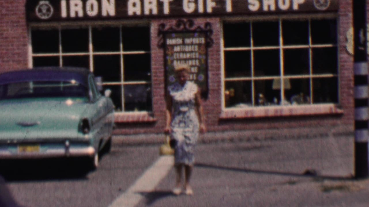 Woman walking near the entrance of Iron Art Gift Shop with a turquoise sedan parked outside.