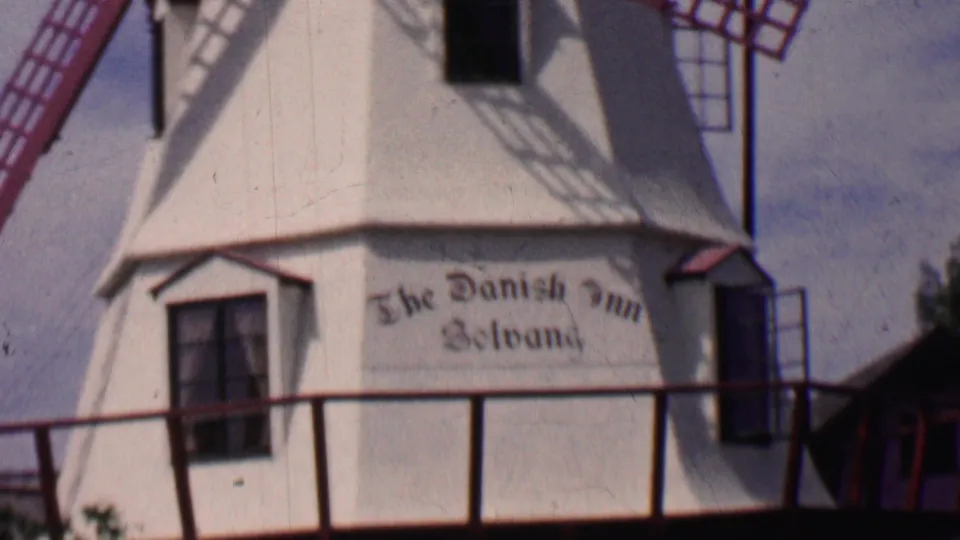 Close 1955 Solvang view of the windmill body, red trim, shadowed window, and readable The Danish Inn Solvang lettering on the white facade.