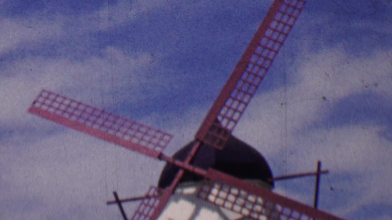 Red-bladed windmill partly cropped against cloudy blue sky.