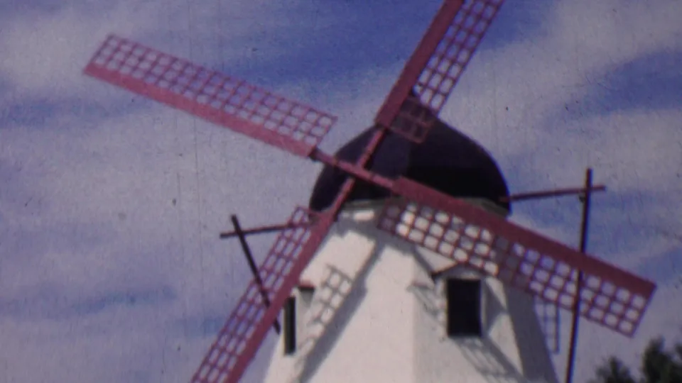 1955 Solvang home-movie frame showing the windmill from below, with red blades crossing the sky and dark trees along the lower edge.