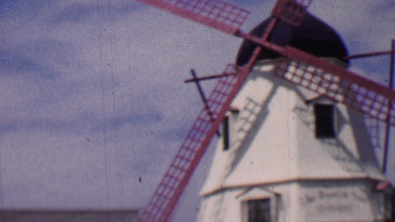 1955 Solvang, California 8mm frame showing a white windmill with red blades and soft blue sky behind it.