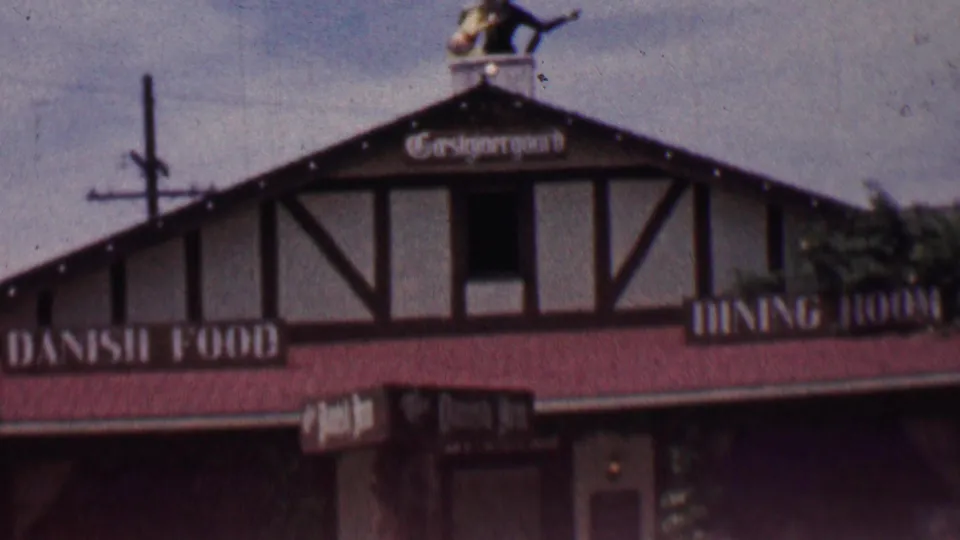 1955 Solvang, California frame with a closer view of the half-timbered restaurant front, Danish Food sign, red roof, rooftop figure, and chimney.