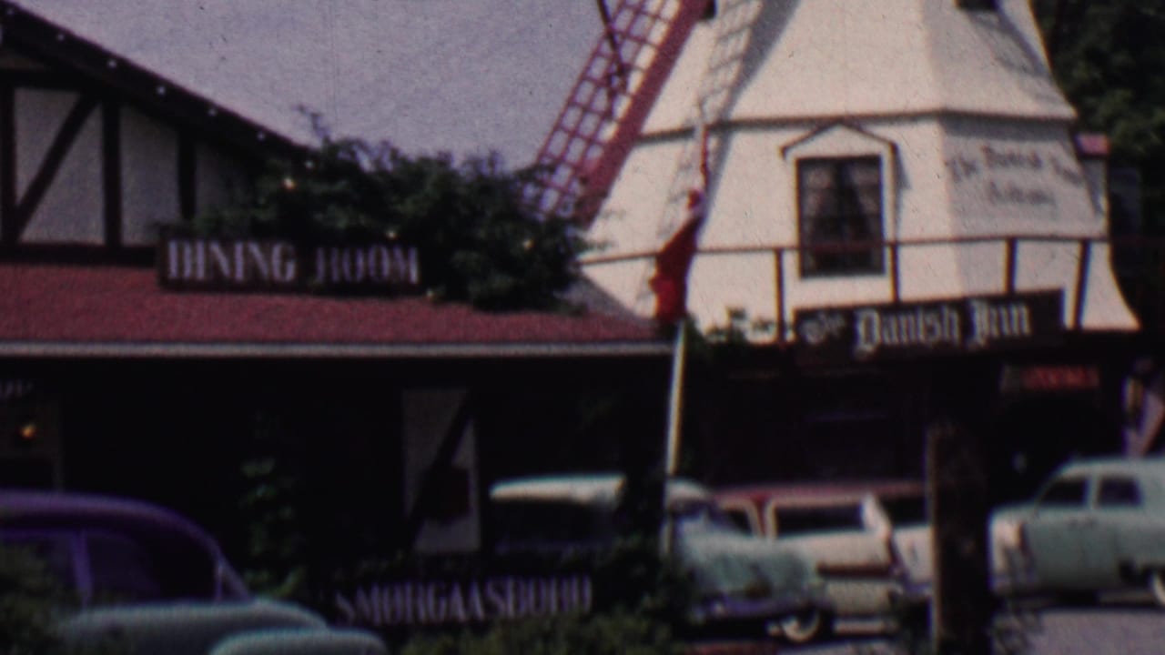 Solvang, California 1950s street view showing the Danish Inn and windmill-style architecture beside parked cars and a visible Old Mission Santa Ines directional sign.