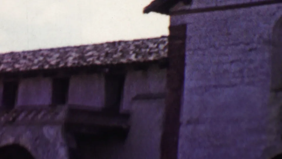 1955 Solvang frame with the camera shifted across a tiled roofline, dark upper windows, a small balcony, and a taller stucco wall at the right edge.
