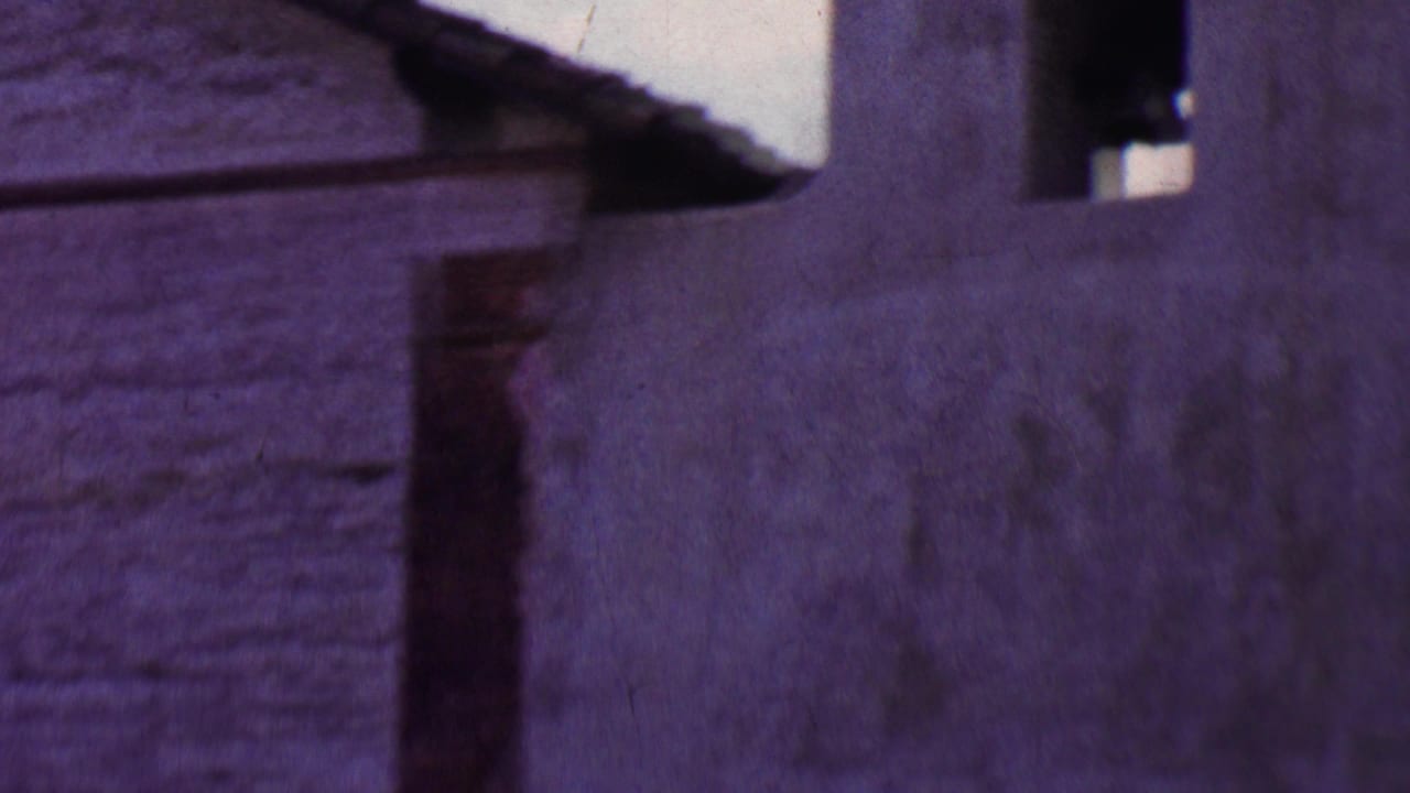 1955 Solvang 8mm frame showing a close, soft-focus view of a weathered stucco church or mission-style wall with dark arched bell openings.