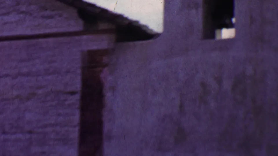 1955 Solvang 8mm frame showing a close, soft-focus view of a weathered stucco church or mission-style wall with dark arched bell openings.