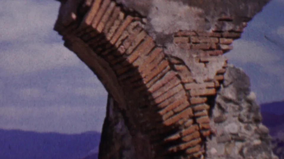 1955 8mm frame from Solvang, California, with the damaged brick arch and stone support dominating the view above a distant landscape.