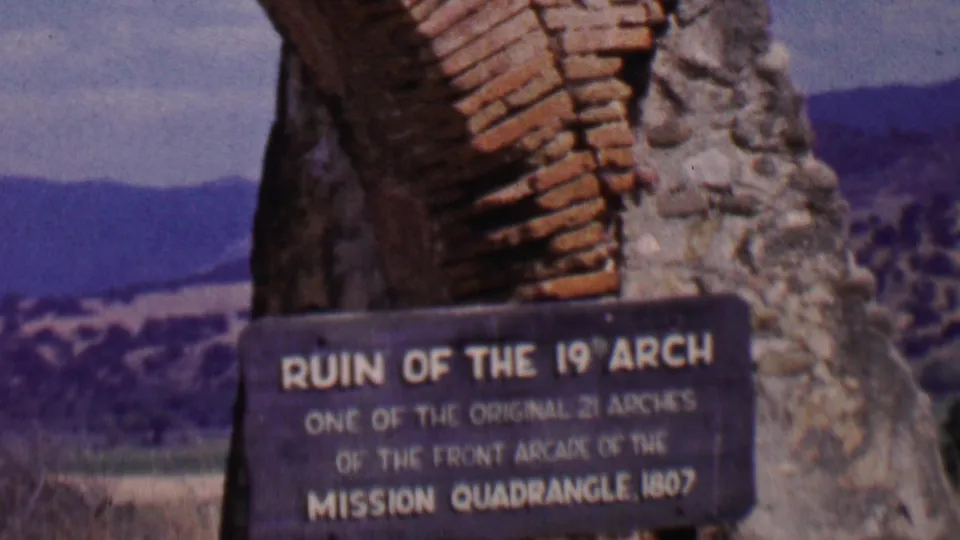 1955 Solvang, California, frame showing the ruin of the 19th arch with a readable historical plaque and distant hills beyond the masonry.