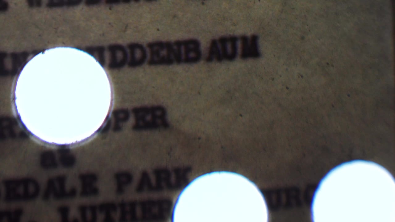 Soft 8mm close-up of a typewritten wedding invitation for the supplied 1950 Detroit wedding context, partly obscured by a bright circular flare and heavy grain.