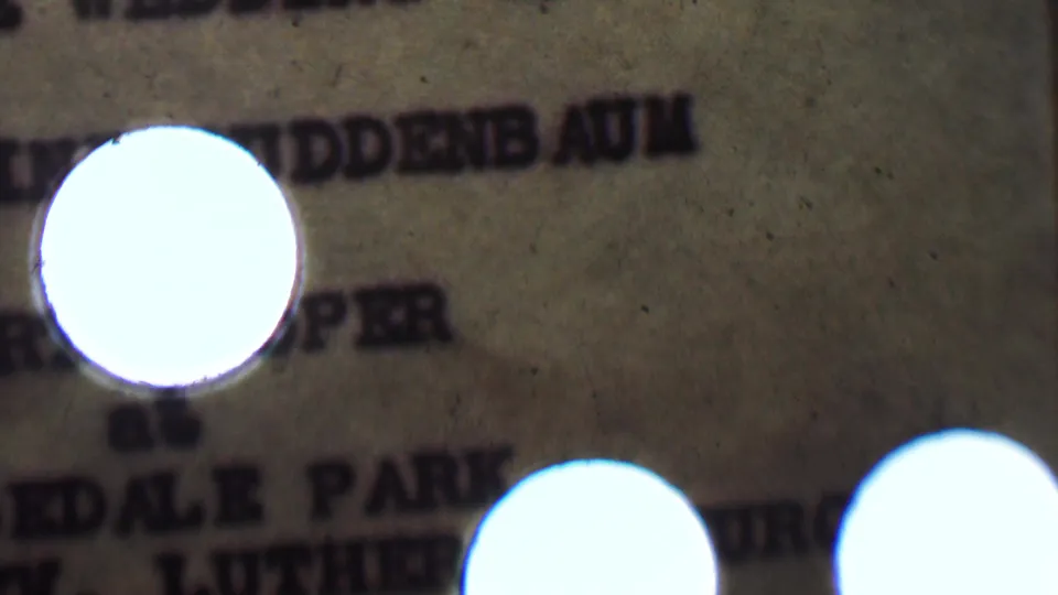 Soft 8mm close-up of a typewritten wedding invitation for the supplied 1950 Detroit wedding context, partly obscured by a bright circular flare and heavy grain.