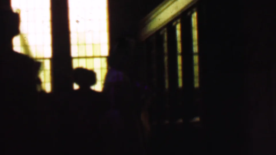 The clip ends on a dark interior or shaded entryway with silhouetted people beside bright window panels, suggesting a transition from the exterior street scene.