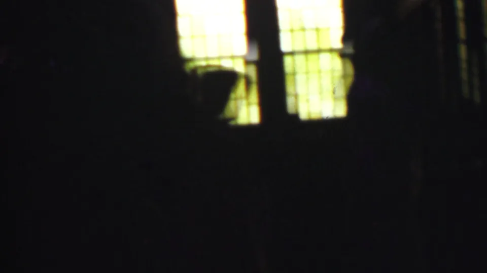 Several dark human forms are faintly visible against glowing grid-patterned church windows, with the surrounding interior falling into deep shadow.