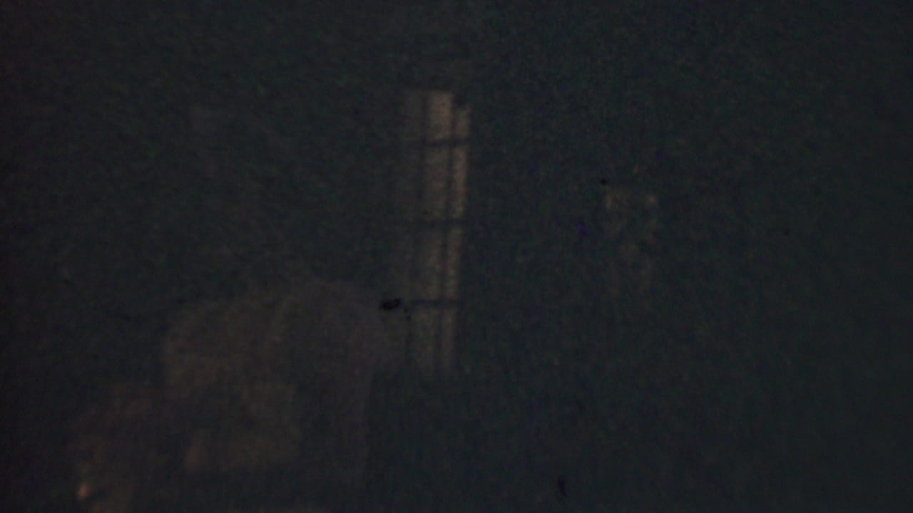 Extremely dark 1950 Detroit 8mm frame with a barely visible woman near a dim vertical window light and heavy film grain.