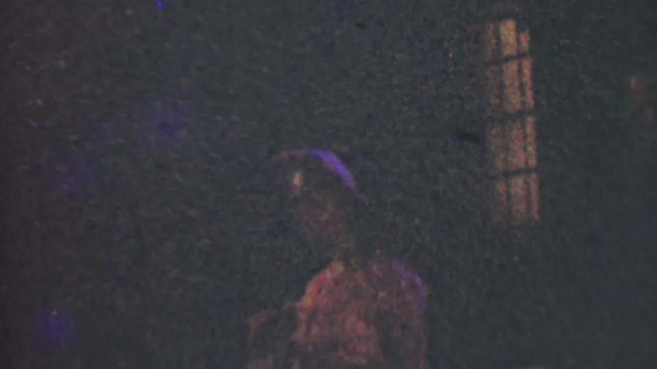Very dark 1950 Detroit home-movie frame with a faint figure near the bottom and a dim vertical window shape on the right.