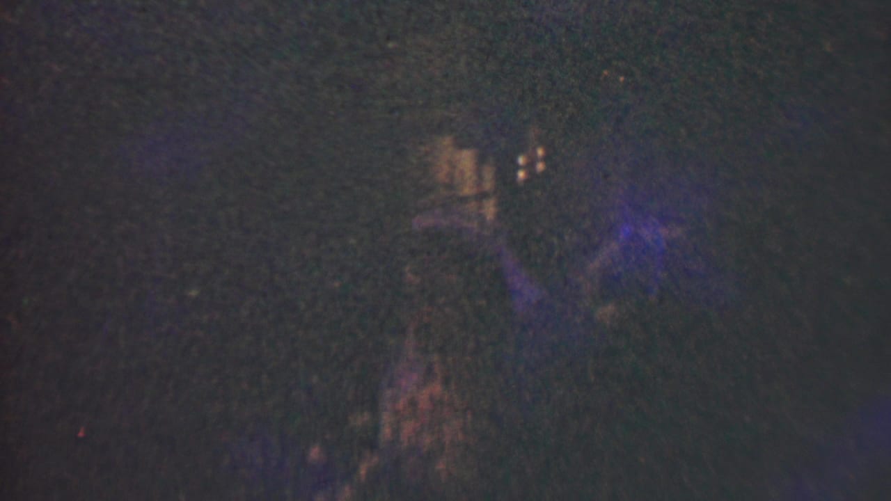 Very dark interior with faint human silhouettes and small warm lights in the background.