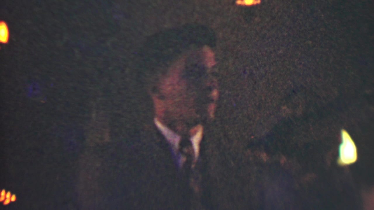Man in a dark suit stands in a low-light formal event scene.