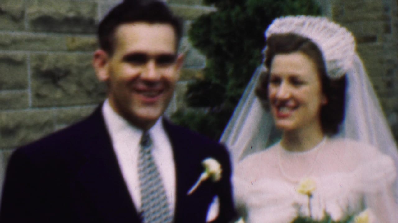 In Detroit, Michigan, 1950, a groom in a dark suit and patterned tie smiles beside a bride wearing a white dress, veil, and floral headpiece outside a stone church.