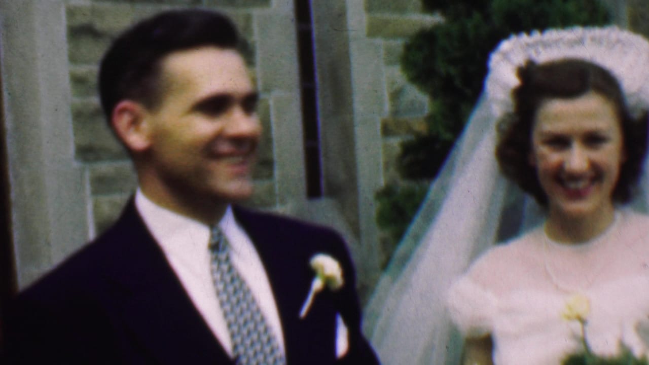Groom and bride smile while standing side by side outside a stone church entrance.