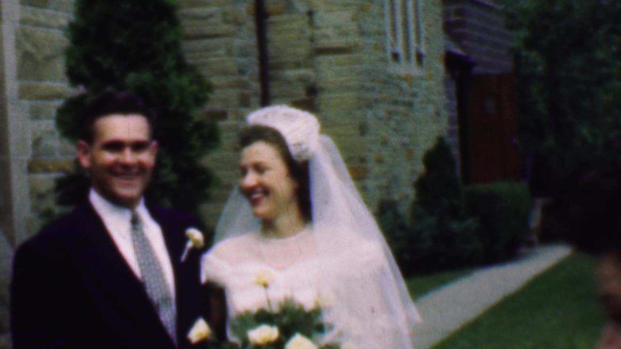 In 1950 Detroit home-movie footage, a bride in a white veil and a groom in a dark suit smile while walking outside a stone church.