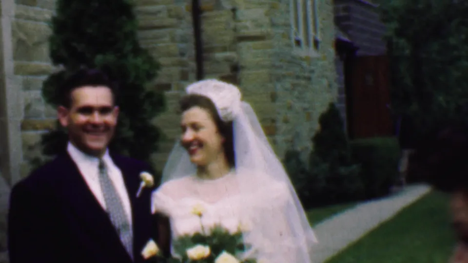 In 1950 Detroit home-movie footage, a bride in a white veil and a groom in a dark suit smile while walking outside a stone church.