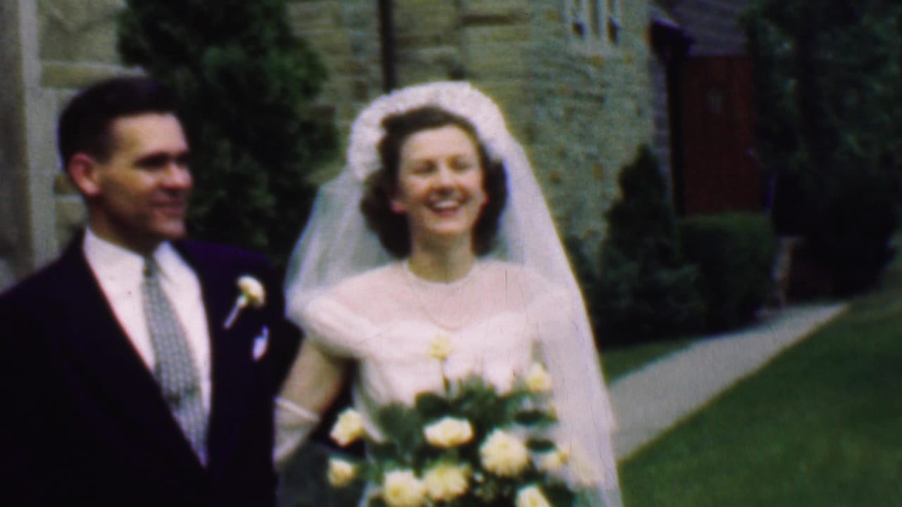 Bride and groom walk together outside a stone church, both smiling.