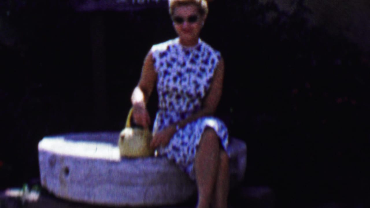 Woman in sunglasses seated on a stone millstone with a basket beside her.