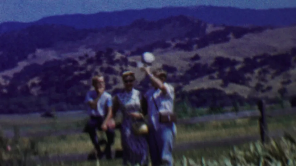 In the supplied 1955 Solvang, California home-movie context, a family group stands near a fence in dry grass with rural hills and mountains in the background.