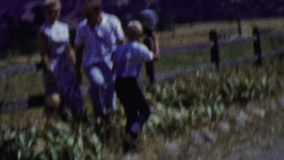 A woman, a man, and a child move near a wooden fence in the supplied Solvang-area setting, with dry grass and a road or path visible behind them.