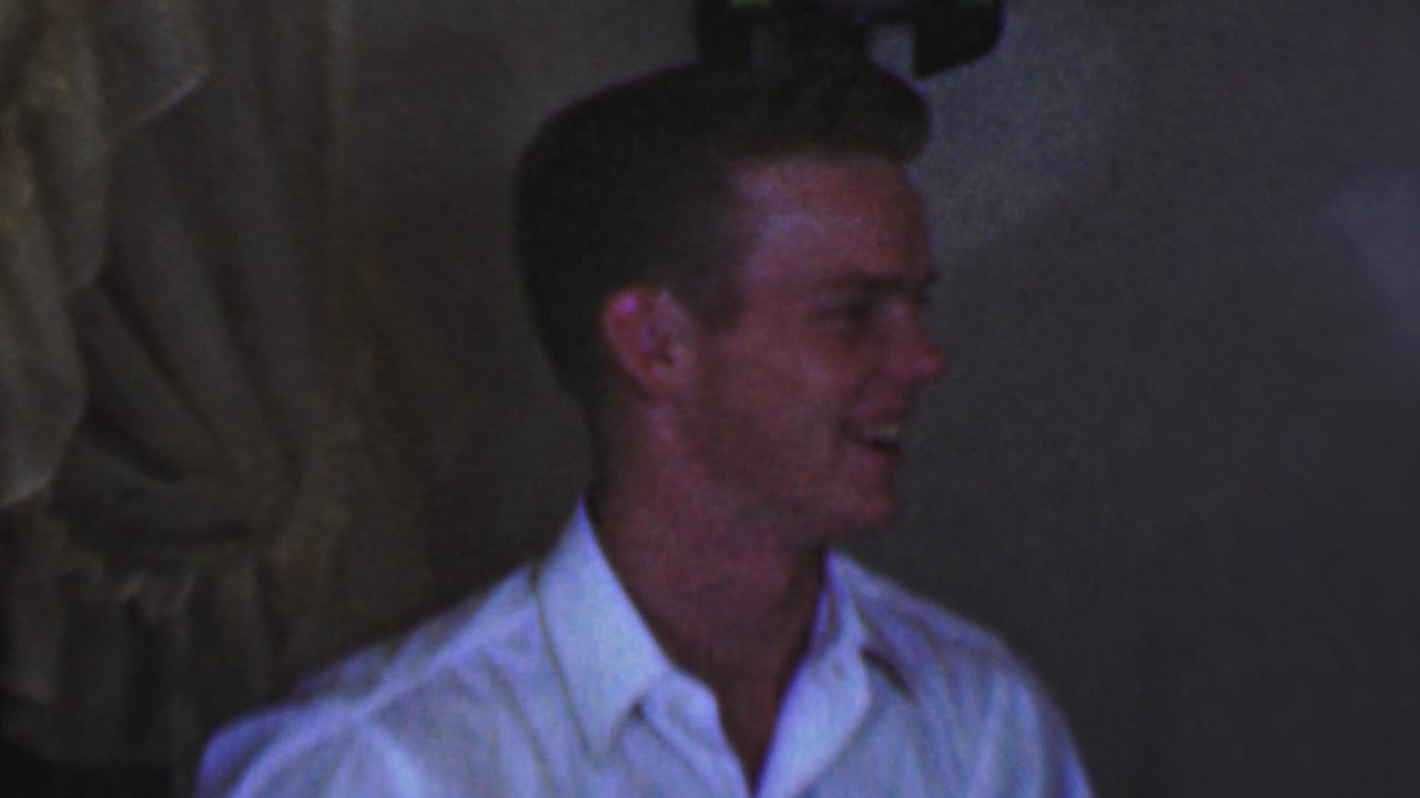 Young male in a white shirt laughs while facing to the side.
